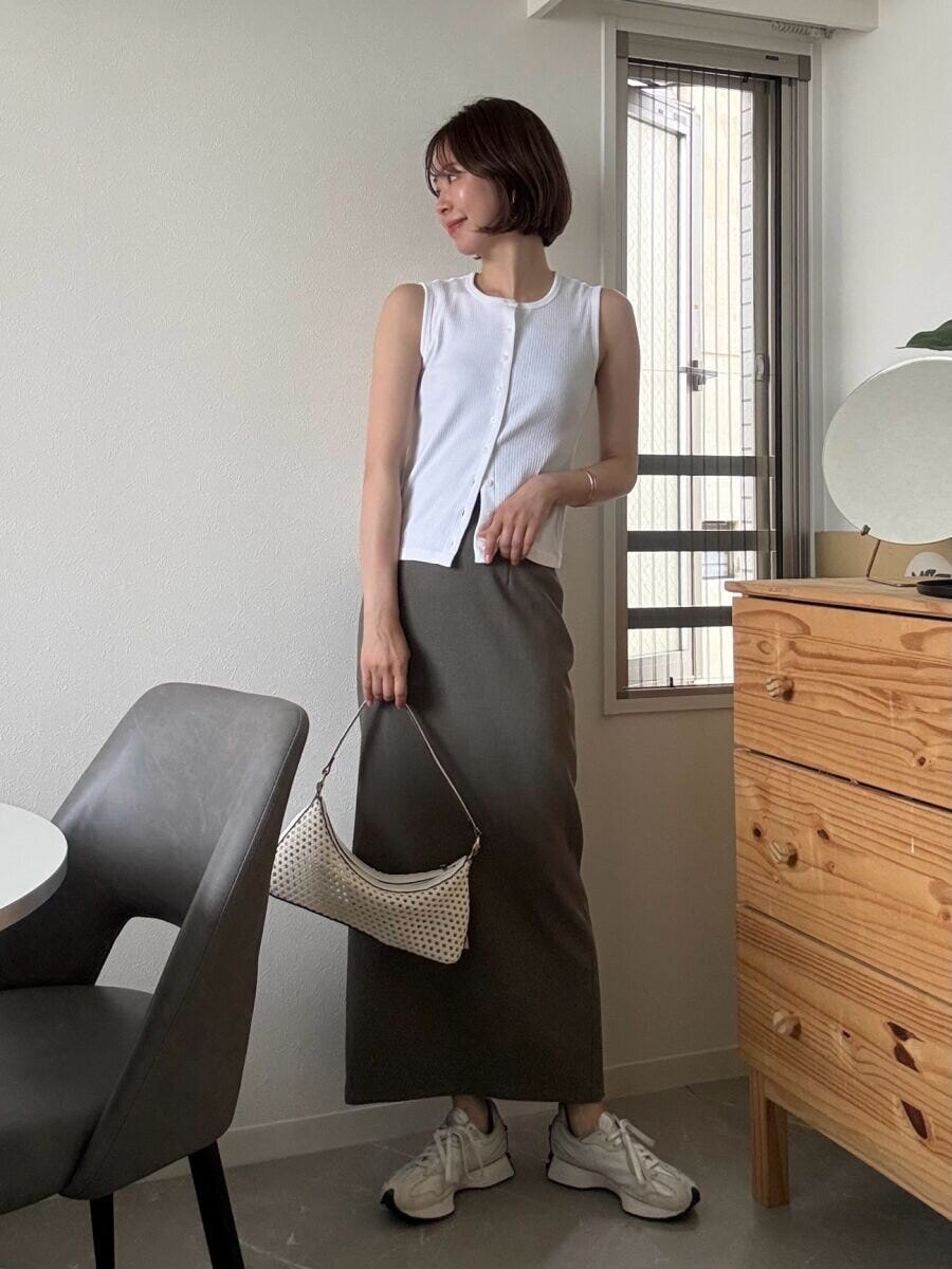 白いノースリーブとIラインスカートの女性が、バッグを持ち窓際に立つ