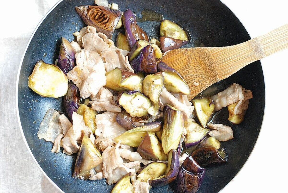 フライパンに戻し入れられ、なすと一緒に炒められている豚バラ肉