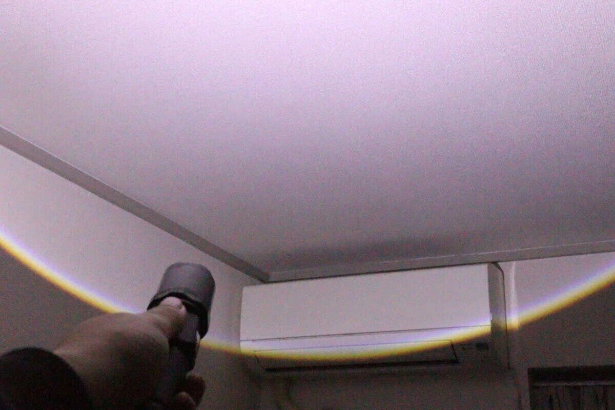 手に持った充電式LEDライトで部屋の天井を照らしている様子