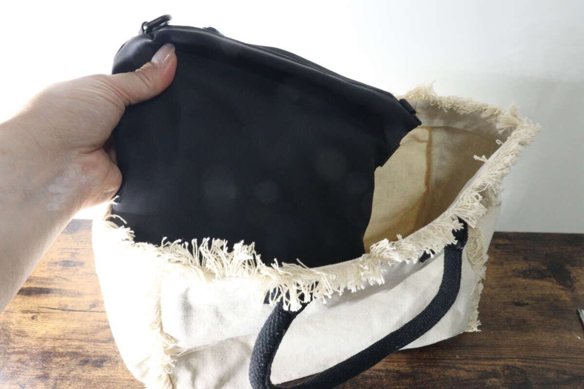 黒いショルダーポーチをトートバッグに入れている手元 黒いショルダーポーチをトートバッグに入れている手元