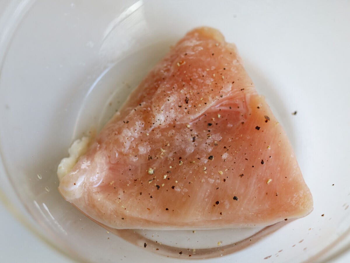 透明なボウルに入った鶏むね肉に、塩こしょうと酒をもみ込んでいる様子