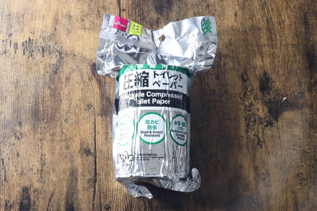 アルミ包装されたダイソーの備蓄用圧縮トイレットペーパーが木目のテーブルに置かれている俯瞰。