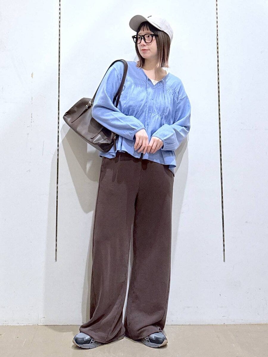 水色のシャーリングニットを着た女性がキャップとメガネで立つ