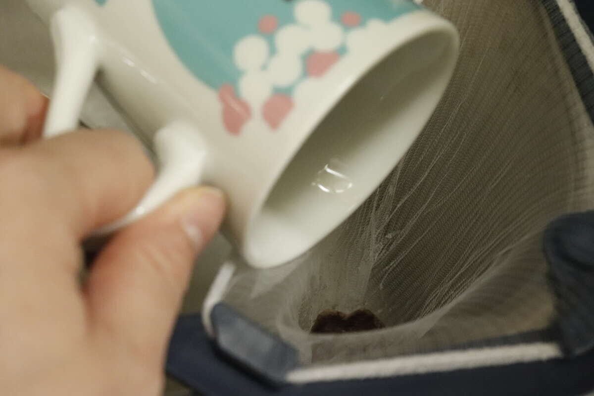 水切りネットにコーヒーかすをカップから捨てている手元