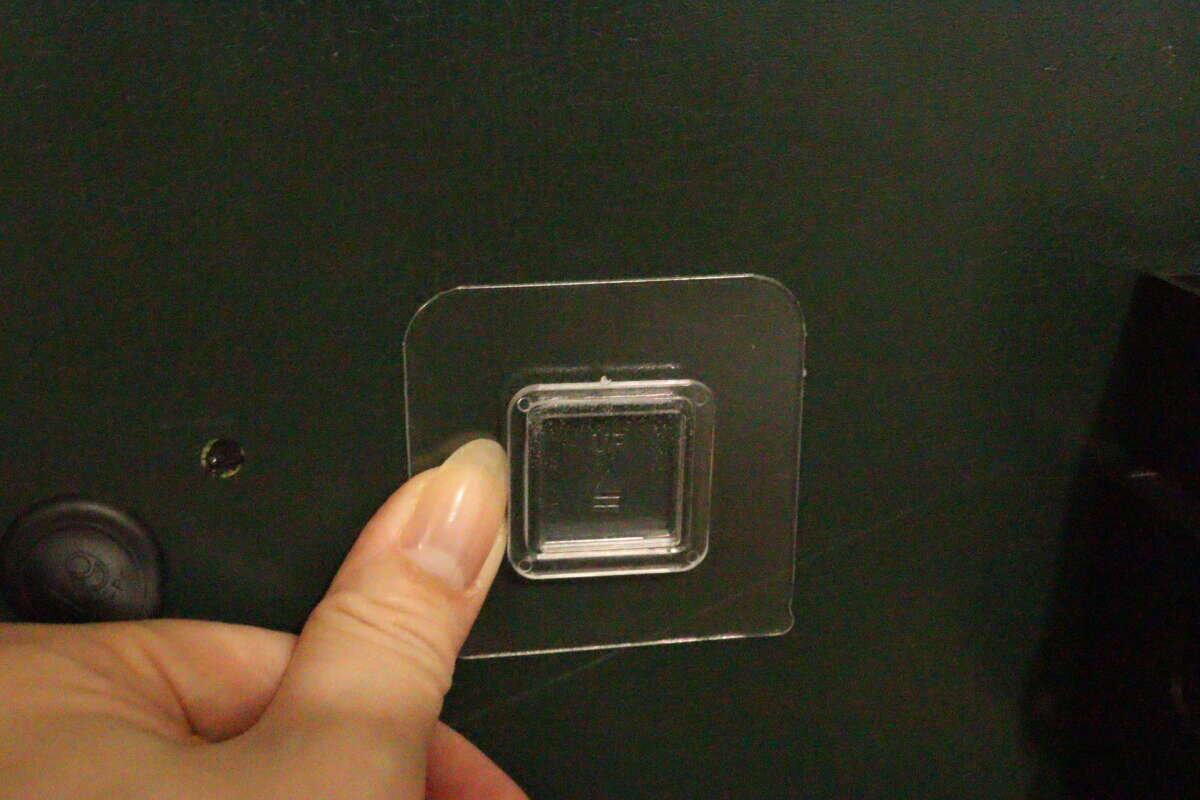 濃い緑色の壁に透明な粘着シートを指でしっかりと押し付けている様子