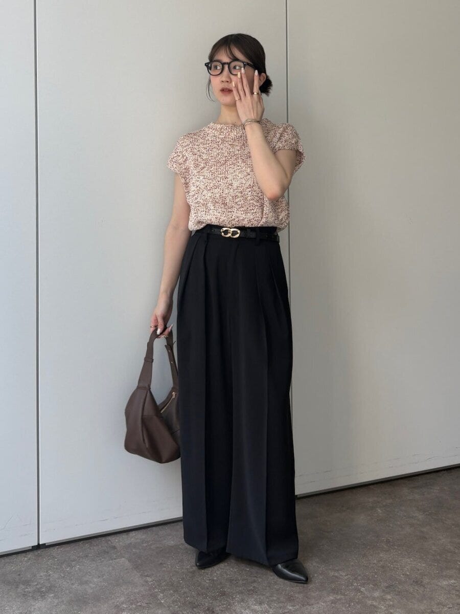 眼鏡の女性がピンクニットと黒ワイドパンツでポーズ