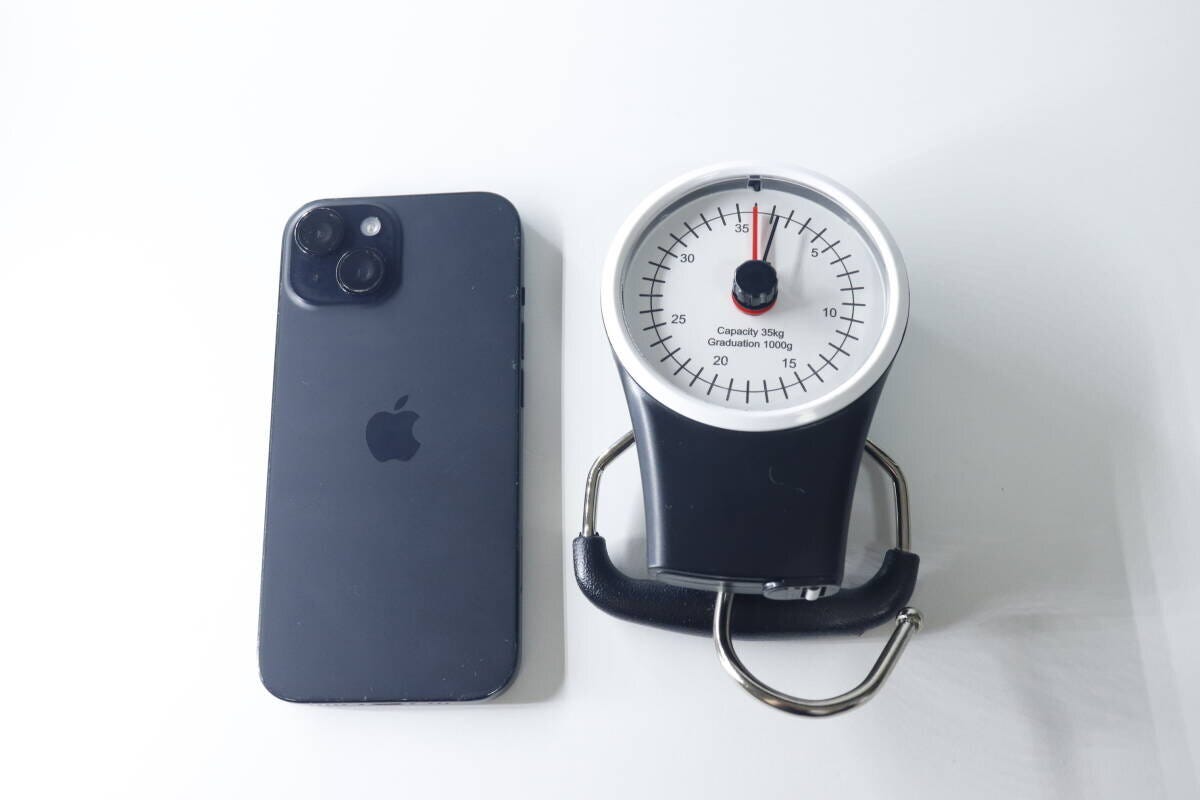 黒いスマートフォンと並べて置かれたスーツケース用計り。計りの方が大きい。