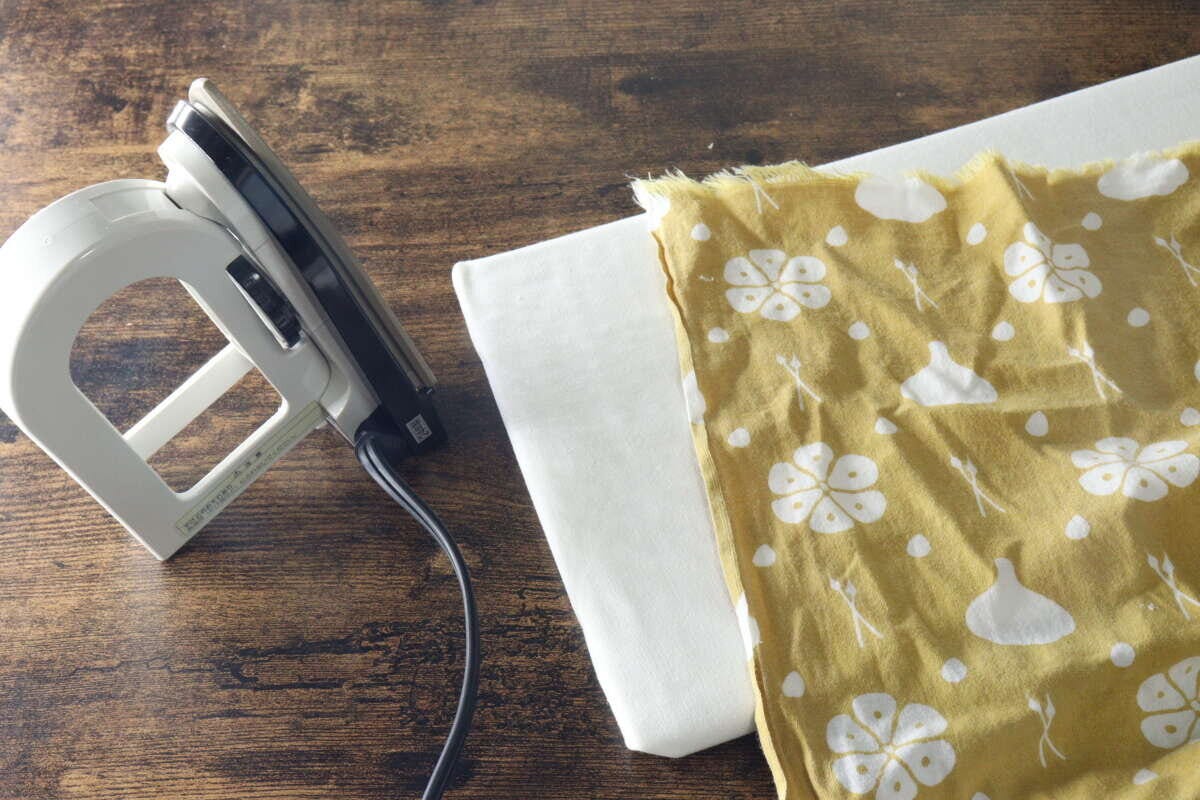 ミニアイロン台とアイロン、黄色の花柄の布が木製テーブルに並べられている