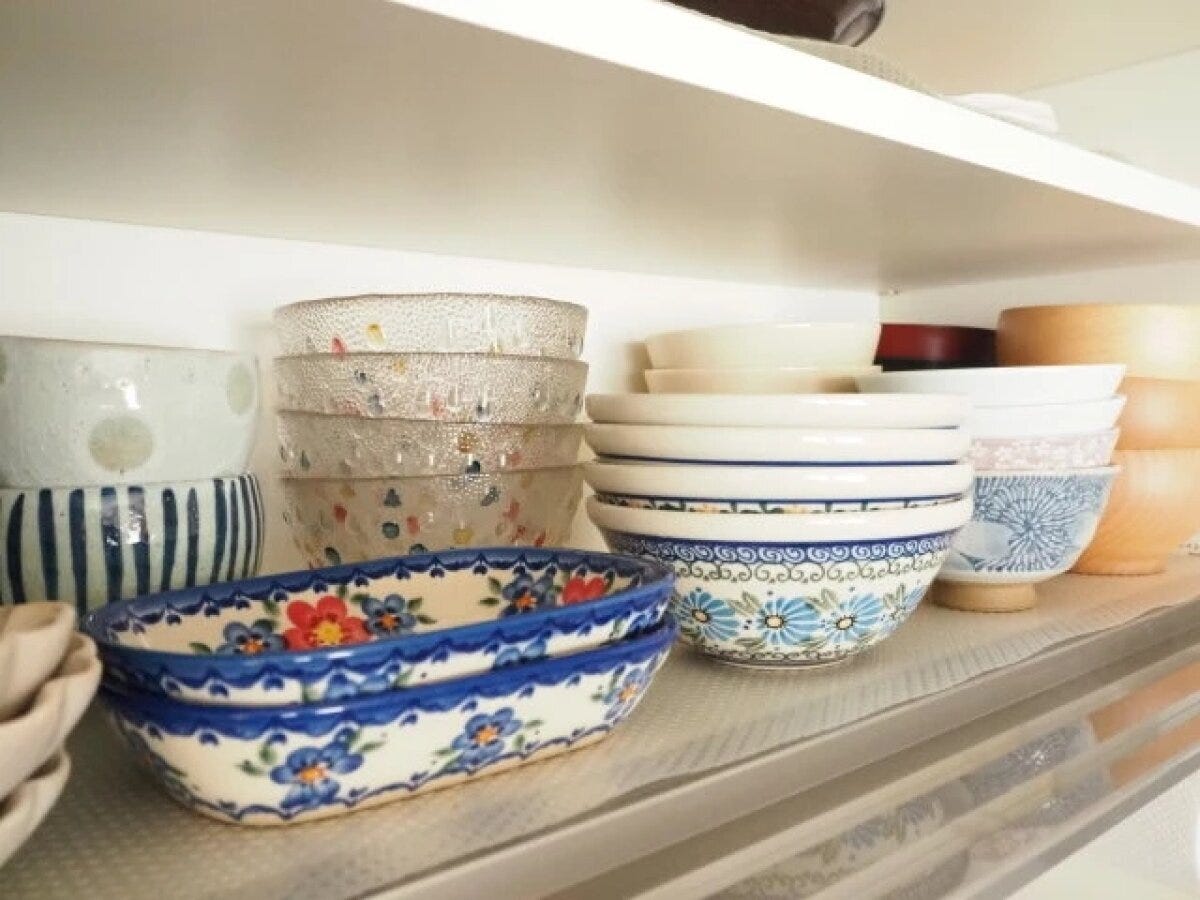 食器棚の棚に様々なデザインの茶碗や小鉢が並べられている