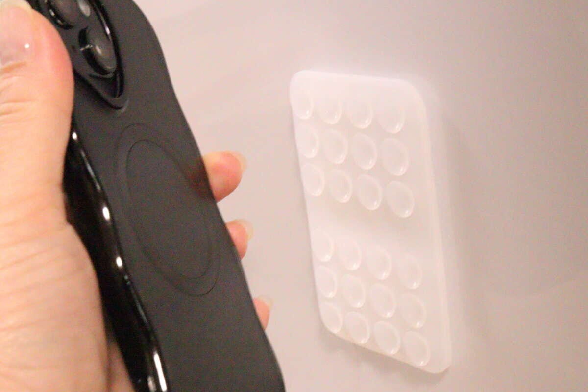 壁に貼られた吸着マットに黒いスマホを近づけている様子