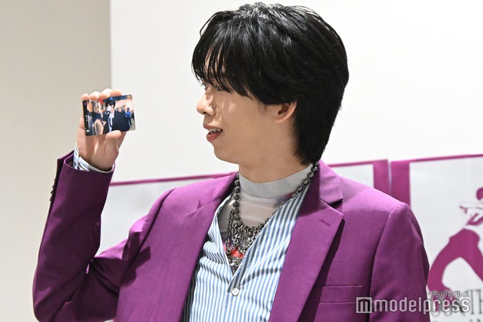 一般通行人としてニュース出演した際の再現ショットトレカを持つリョウガ(C)モデルプレス