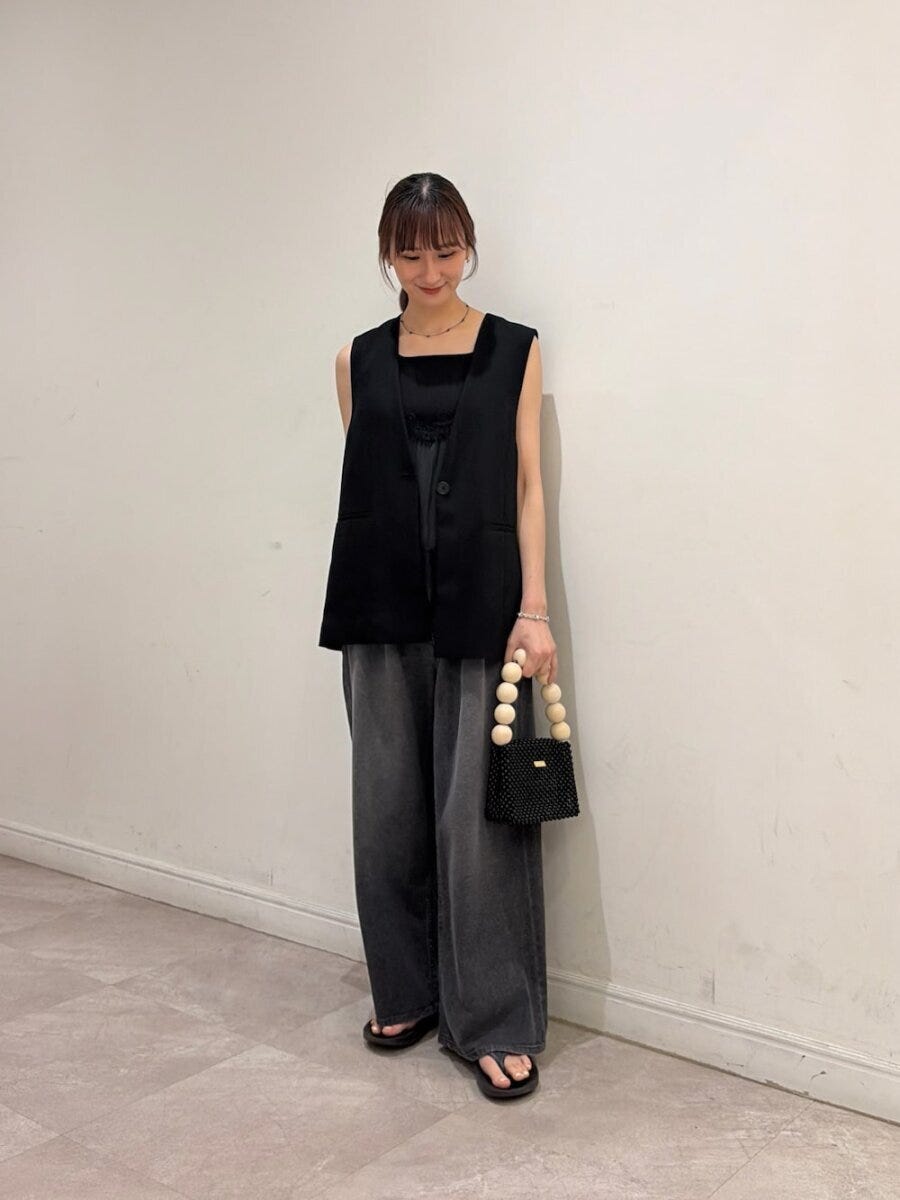 黒いジレと黒いワイドデニムを着用し、ビーズバッグを持った女性 黒いジレと黒いワイドデニムを着用し、ビーズバッグを持った女性