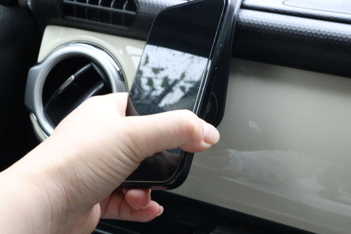 女性の手がスマートフォンを車載ホルダーのマグネット部分に固定している 女性の手がスマートフォンを車載ホルダーのマグネット部分に固定している