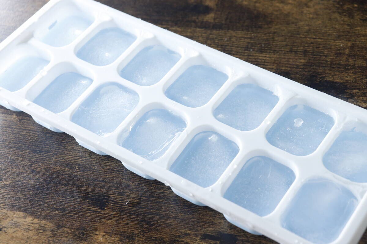 水が凍って氷になった状態のアイストレーが木目のテーブルに置かれている 水が凍って氷になった状態のアイストレーが木目のテーブルに置かれている