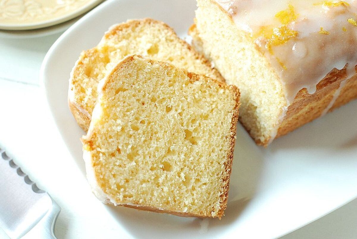 白い皿にアイシングとレモンの皮をのせたヨーグルトレモンケーキと、カットされた2切れの断面を並べた写真
