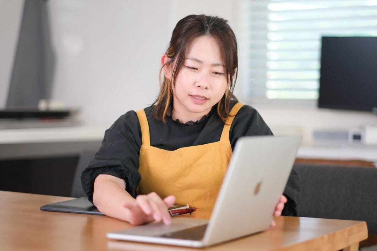 黄色いエプロンの女性が真剣な表情でノートパソコンを操作