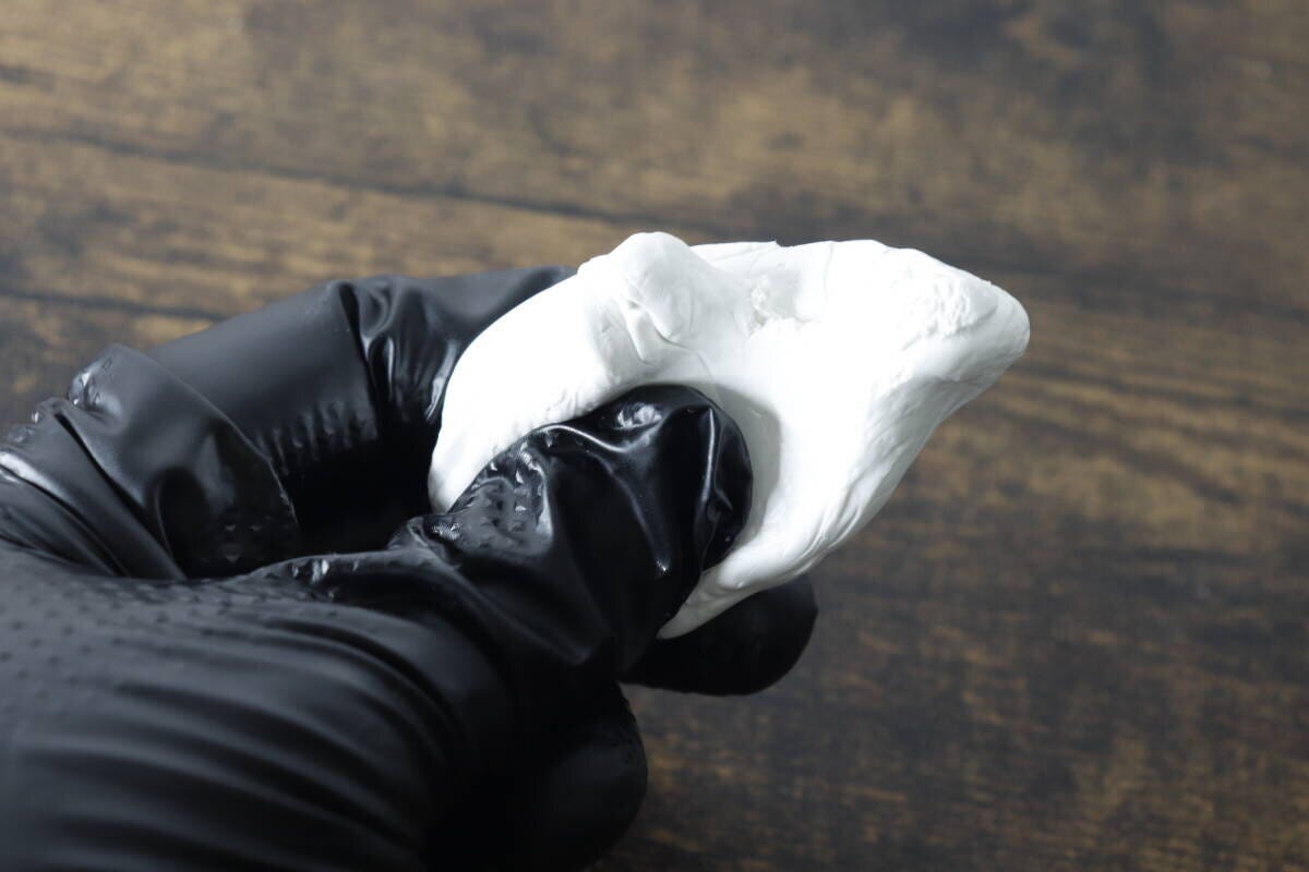 黒いゴム手袋をはめた手で白いすきまパテを練っている様子 黒いゴム手袋をはめた手で白いすきまパテを練っている様子