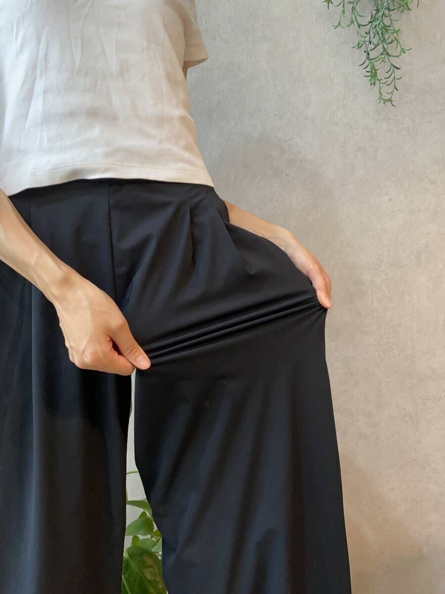 女性が黒いワイドパンツの生地を引っ張りストレッチ性を示している