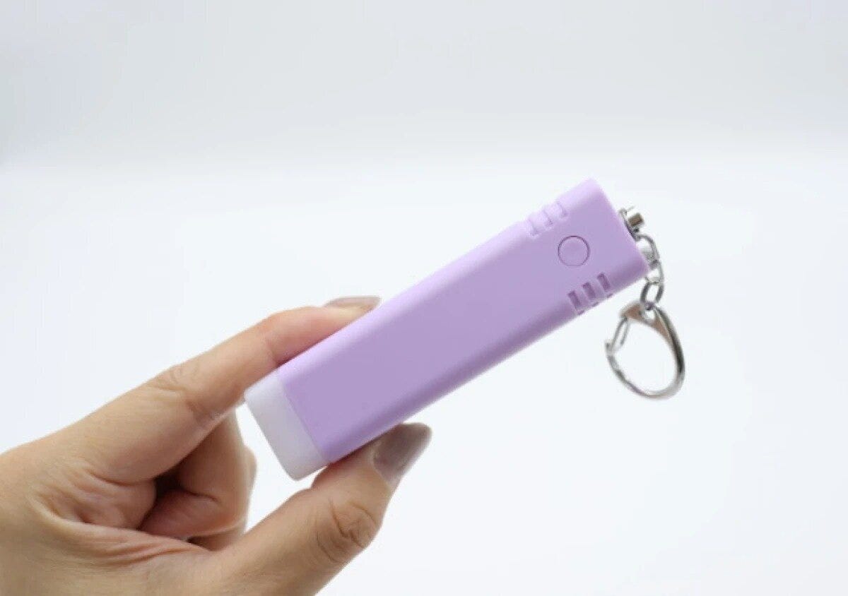 女性が紫色の防犯ブザーを指で挟んで持っている手元 女性が紫色の防犯ブザーを指で挟んで持っている手元