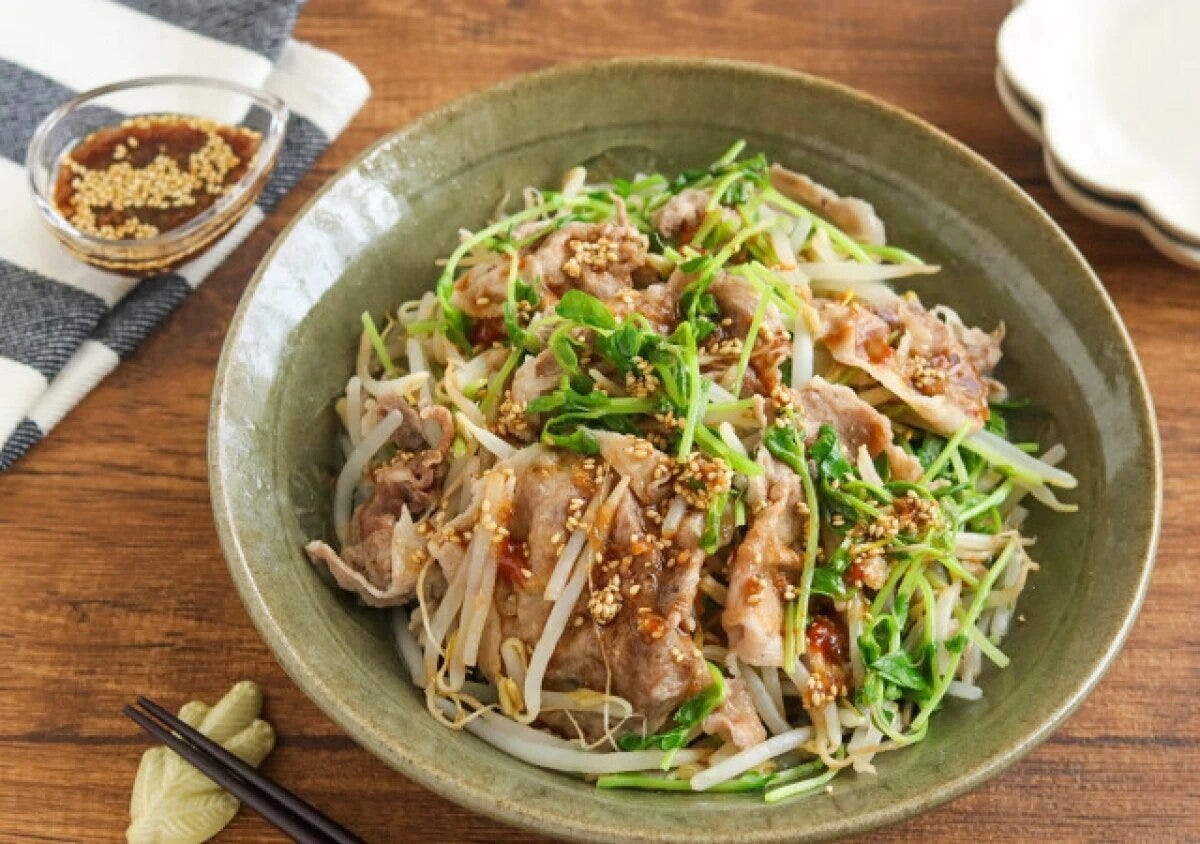 緑の器に盛った豚肉ともやしのレンジ蒸し 緑色の和食器に盛られた豚うす切り肉ともやし、豆苗のレンジ蒸し。白ごま入りのピリ辛中華ダレがかかっている