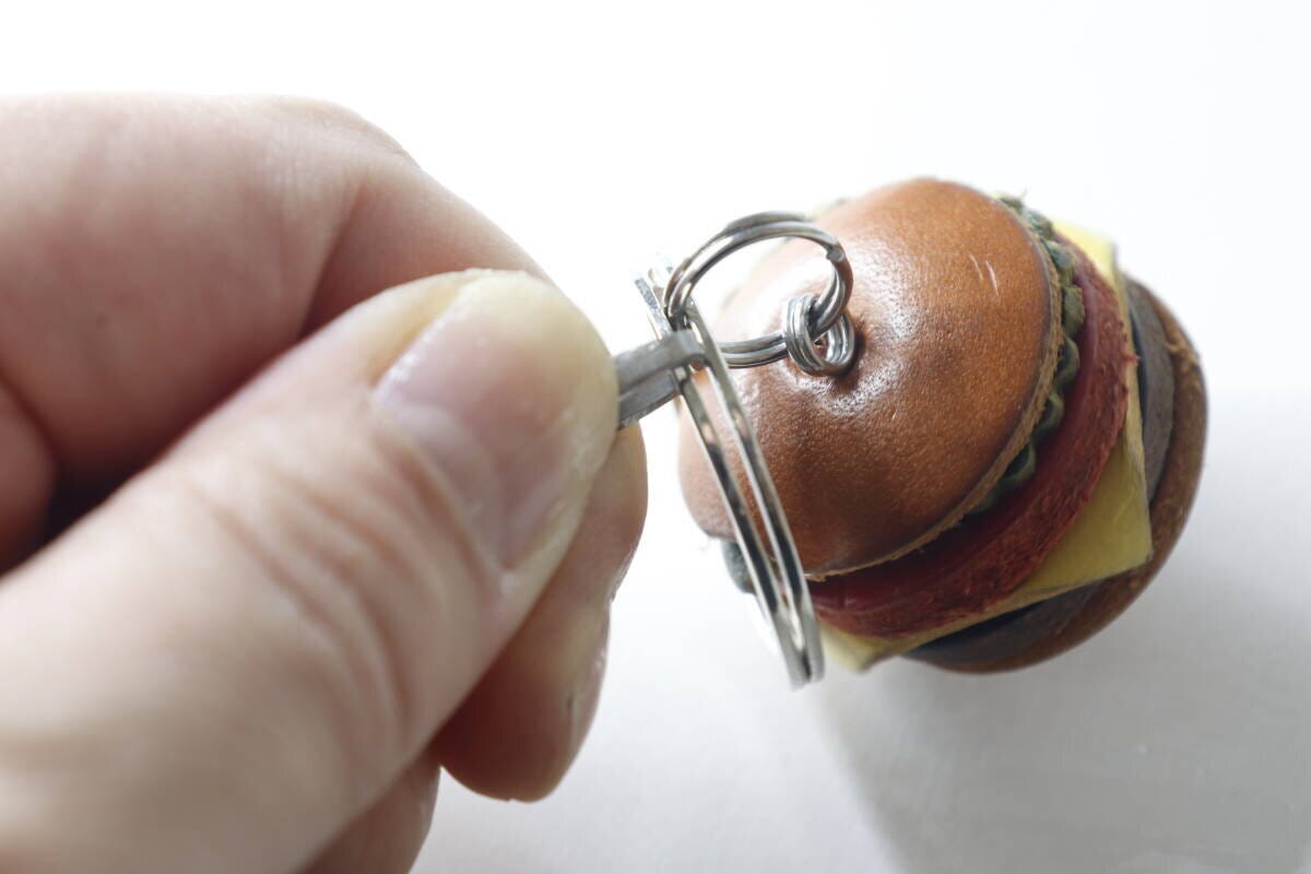 ハンバーガー型キーホルダーのダブルリングにオープナーを差し込む手元 ハンバーガー型キーホルダーのダブルリングにオープナーを差し込む手元