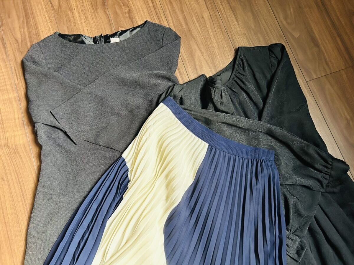 床に広げられたグレーのトップスや黒いブラウスとプリーツスカートなど複数の洋服