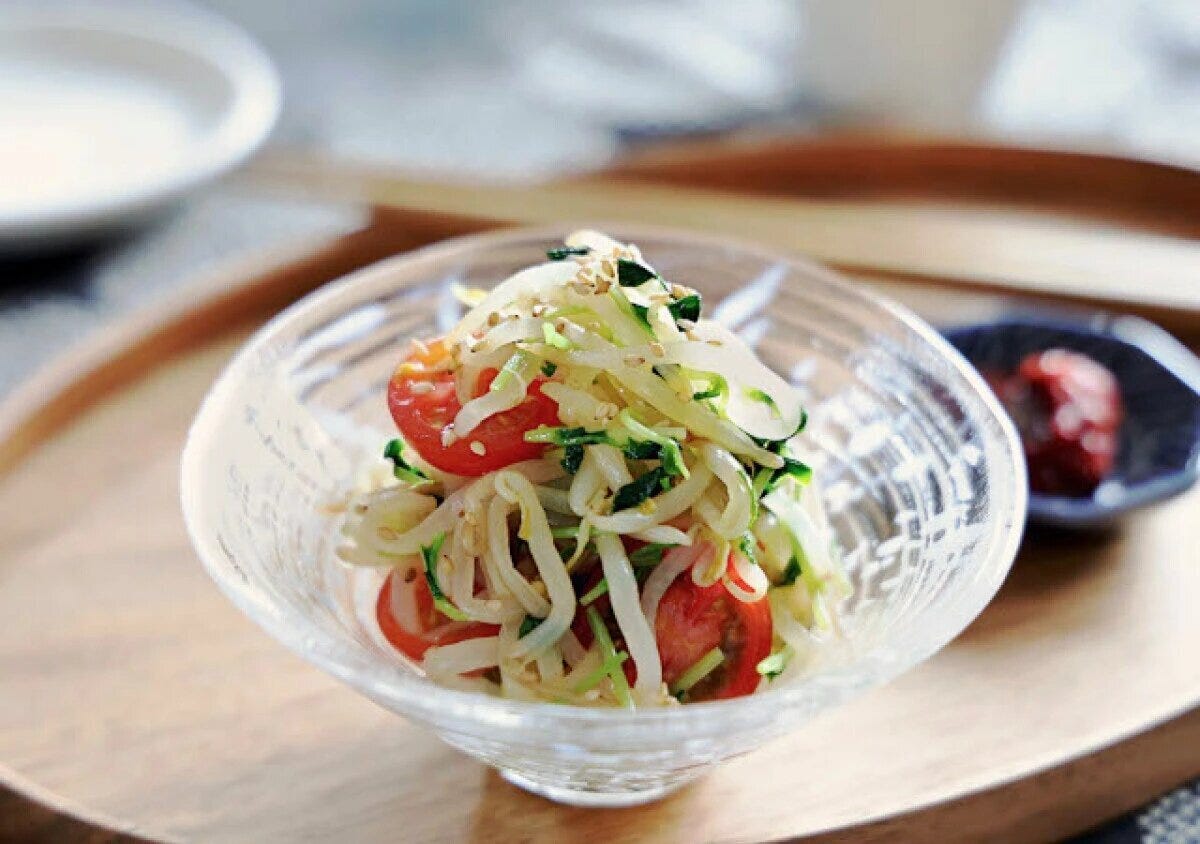 ガラスの器に盛ったもやしとプチトマトのナムル ガラスの器に盛られたもやしと豆苗のナムル。半分に切ったプチトマトと白ごまがのり、木のトレイにのっている