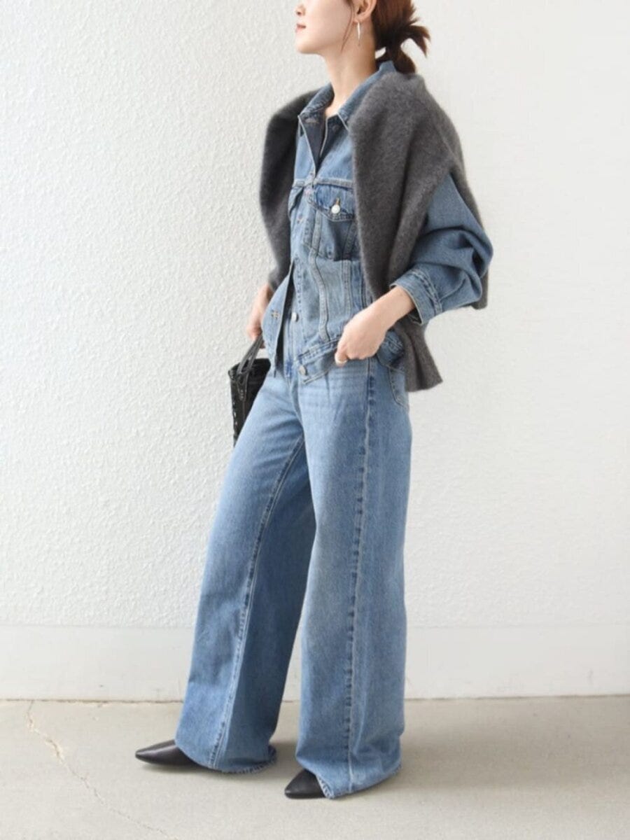デニムオンデニムにグレーのニットを肩掛けしている横向きの女性