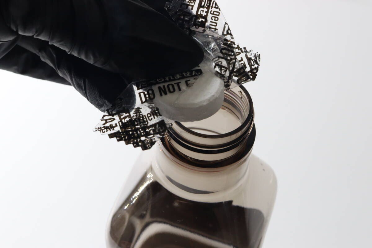黒い手袋をした手でスプレー容器の口に錠剤を入れている様子 黒い手袋をした手でスプレー容器の口に錠剤を入れている様子