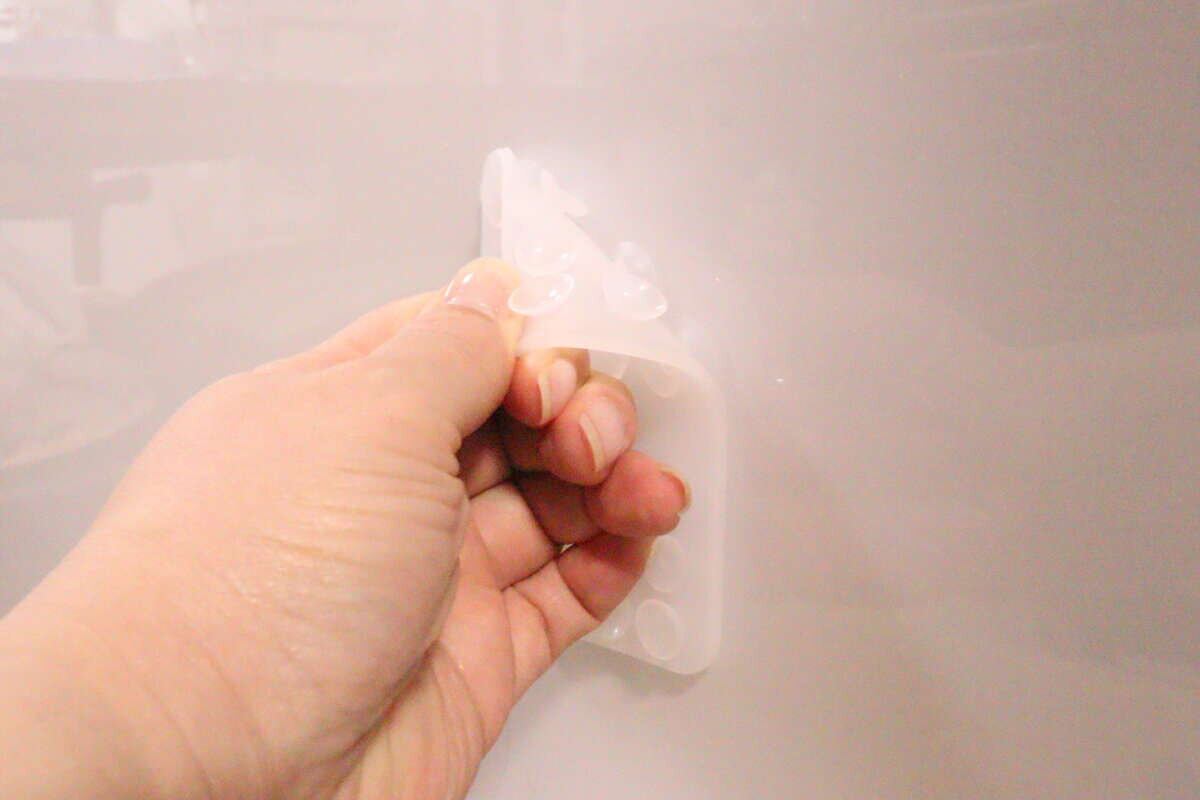 女性の手がシリコン携帯吸着マットを壁に貼り付けている様子