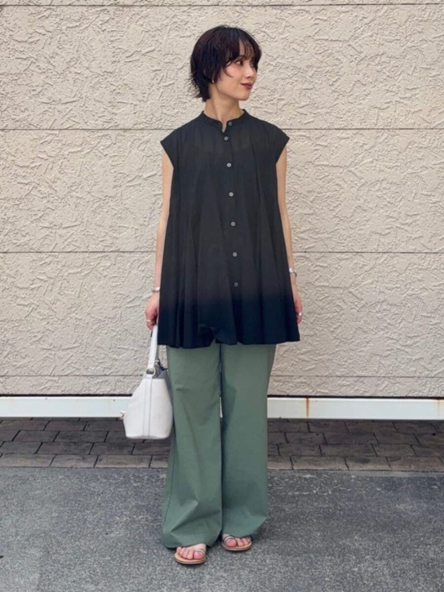 黒ブラウスとカーキパンツの女性が白いバッグを持ち横を向く