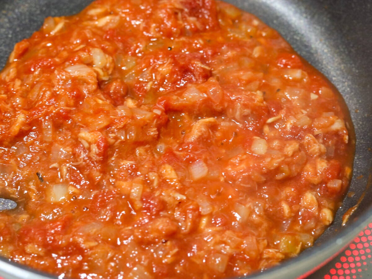 フライパンでホールトマト缶を加えてツナとたまねぎと炒め合わせ中火で煮詰めているトマトソースの工程写真