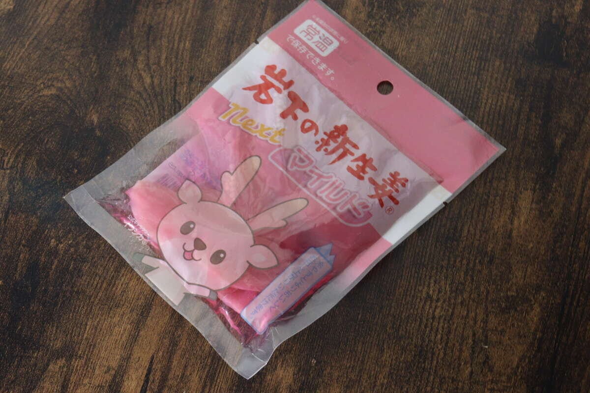 ピンク色のパッケージに入った岩下の新生姜スライスnextが木目のテーブルに置かれている ピンク色のパッケージに入った岩下の新生姜スライスnextが木目のテーブルに置かれている