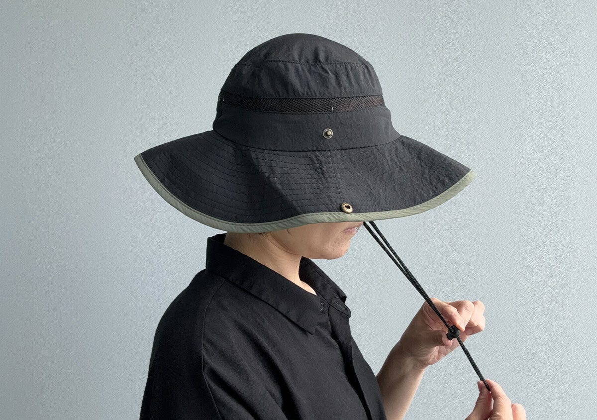 黒いサファリハットを被った女性が顎紐を調整している横顔。