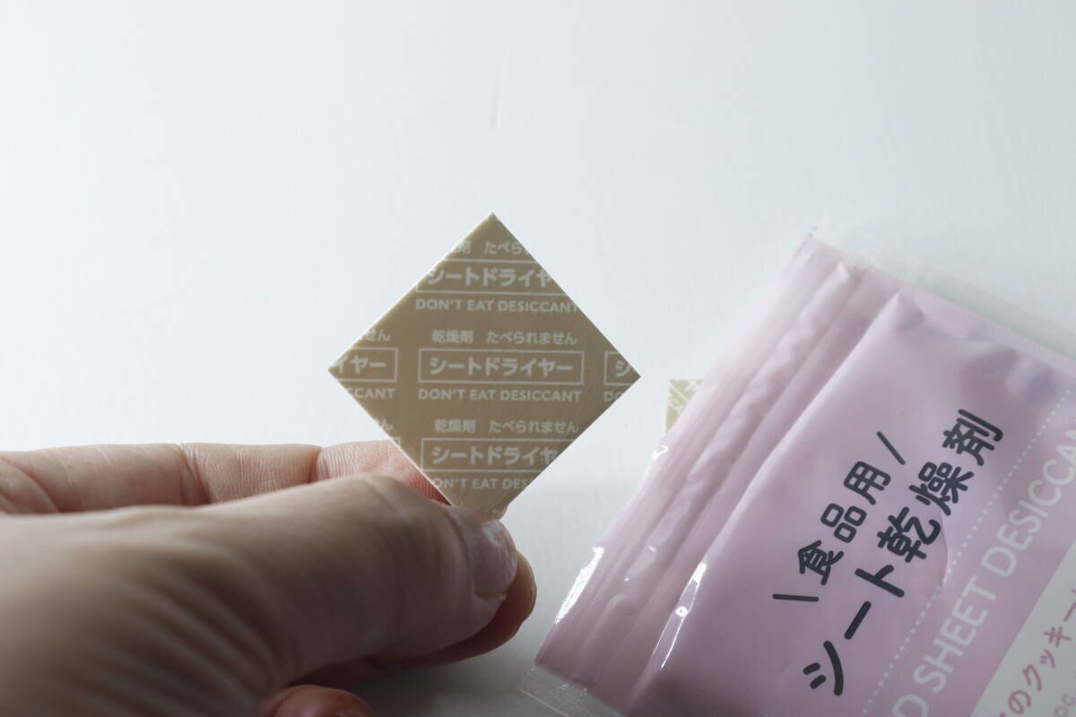 指でつまんだ薄いベージュ色のシート乾燥剤とパッケージの一部