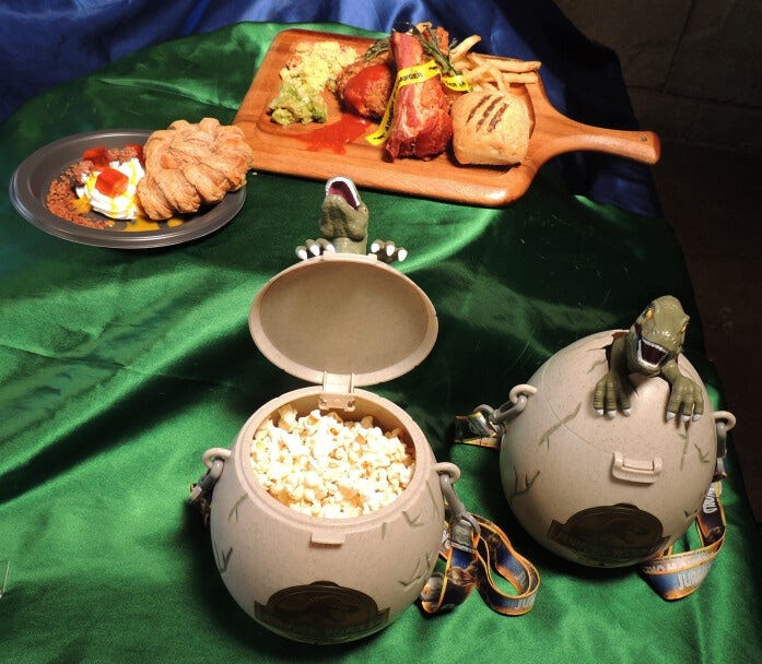 手前は「ポップコーンカート」などで買えるジュラシック・ワールド・ポップコーンバケツ1個4000円。奥は「ロストワールド・レストラン」で販売。右がダイナソー・アタック！ ミートプレート2000円、左がアンモナイトの化石パイ ～レモンクリーム～800円