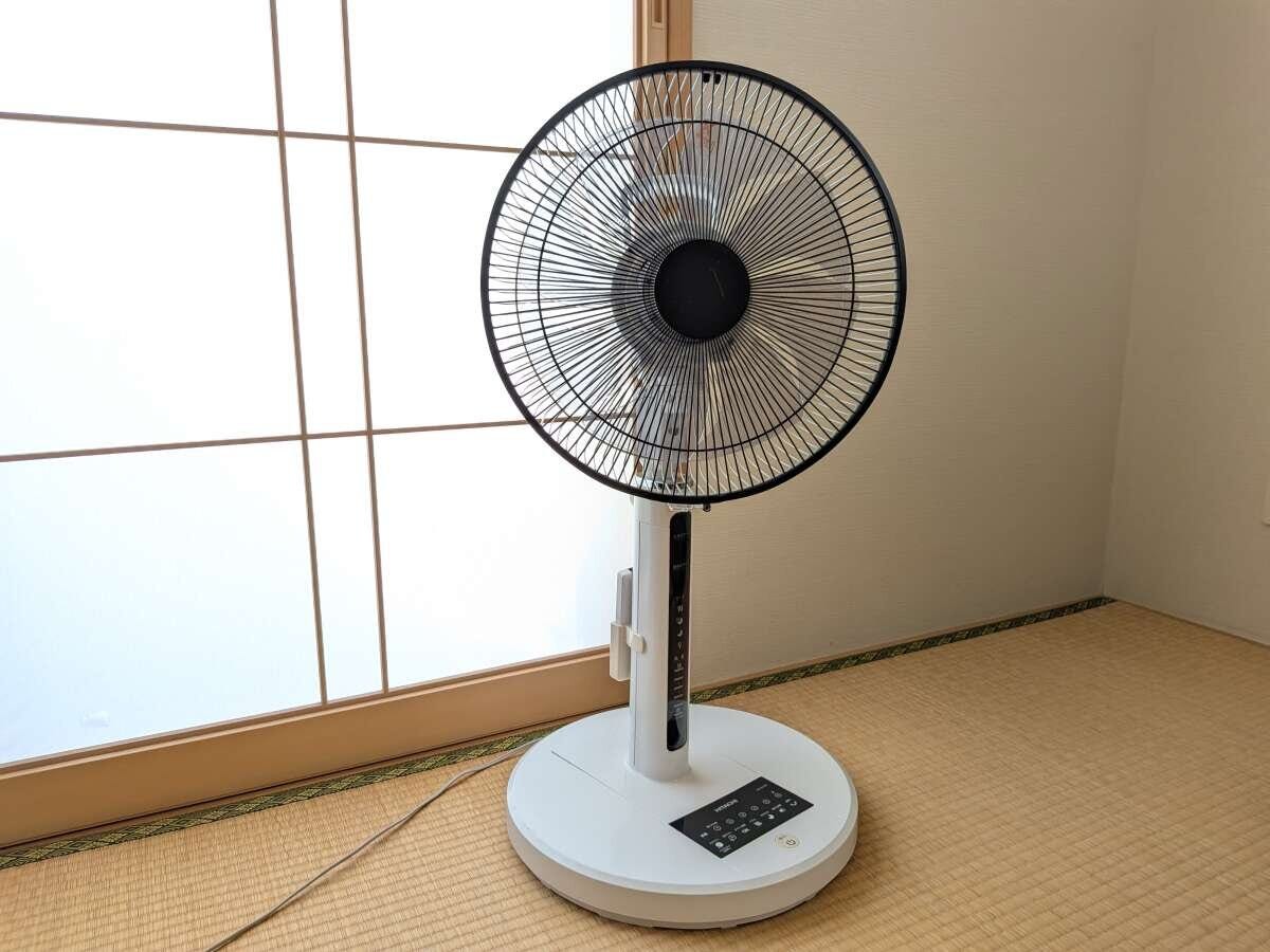 畳の部屋の窓際に置かれた、白い台座と黒い羽根の扇風機