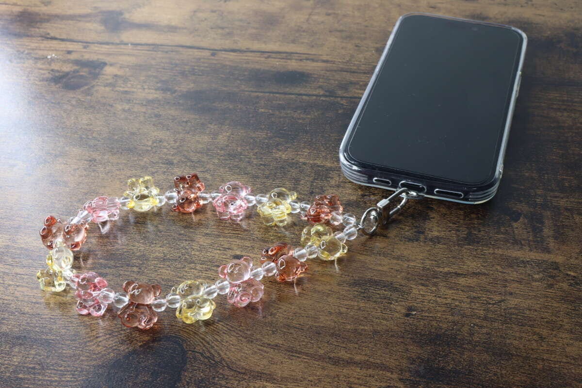 木目のテーブルに置かれたスマホとクマ型ビーズストラップ 木目のテーブルに置かれたスマホとクマ型ビーズストラップ