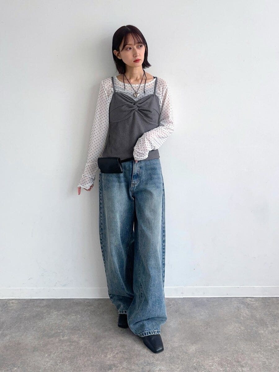 ドット柄シアートップスとビスチェ、ワイドデニムの女性が壁にもたれる