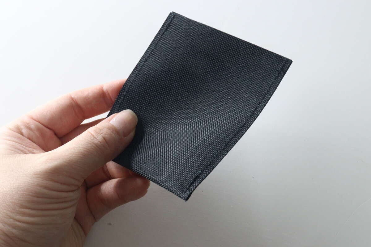 女性の指が黒い布製のポケット本体をつまんでいる 女性の指が黒い布製のポケット本体をつまんでいる