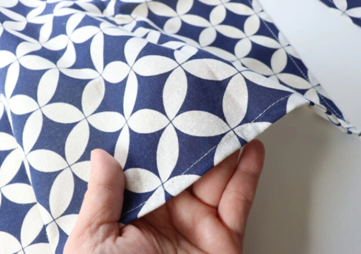 七宝柄の紺色と白の和柄のれんを手で持ち生地の縫製を確認している 七宝柄の紺色と白の和柄のれんを手で持ち生地の縫製を確認している