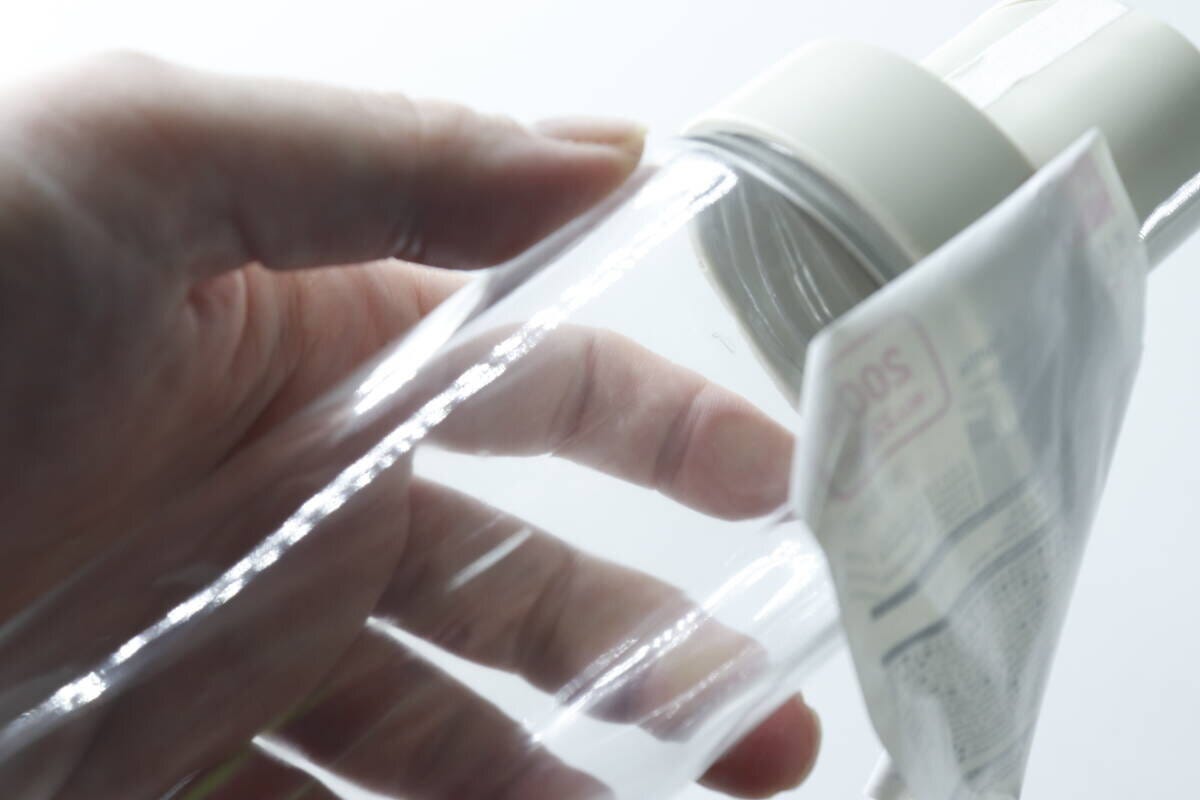 オイルボトルから商品ラベルを剥がしている手のアップ オイルボトルから商品ラベルを剥がしている手のアップ