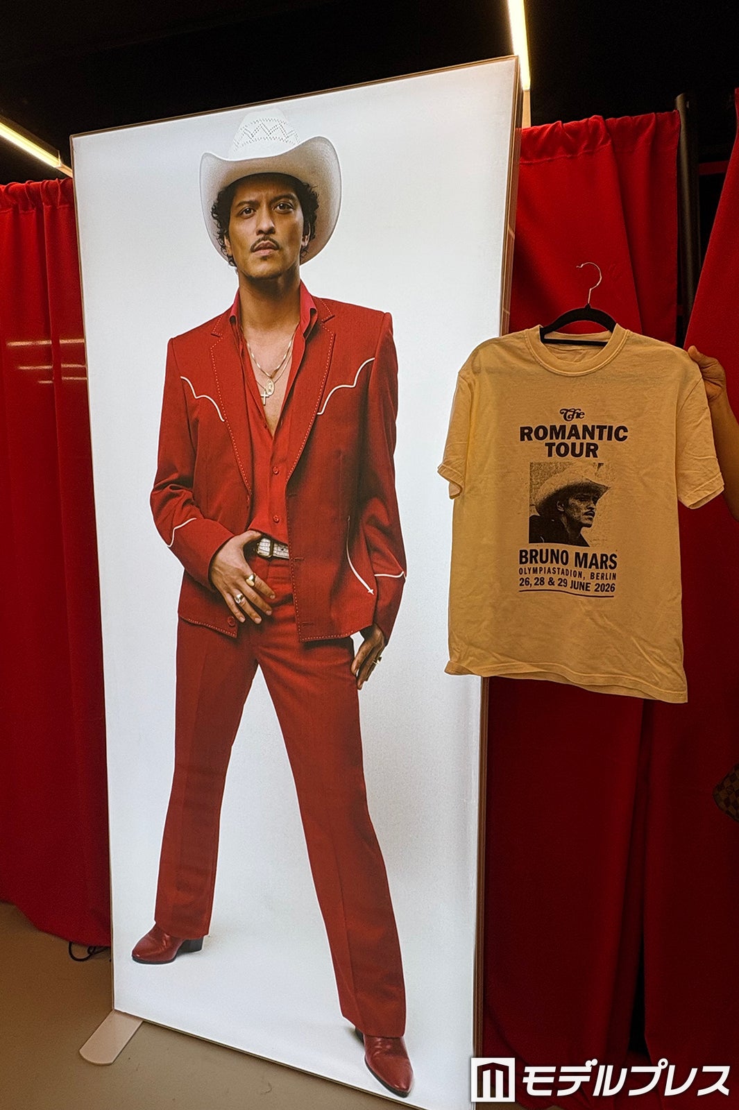 大きく飾られたブルーノ・マーズの写真パネルの前で記念撮影／右はベルリン公演限定Tシャツ（C）モデルプレス