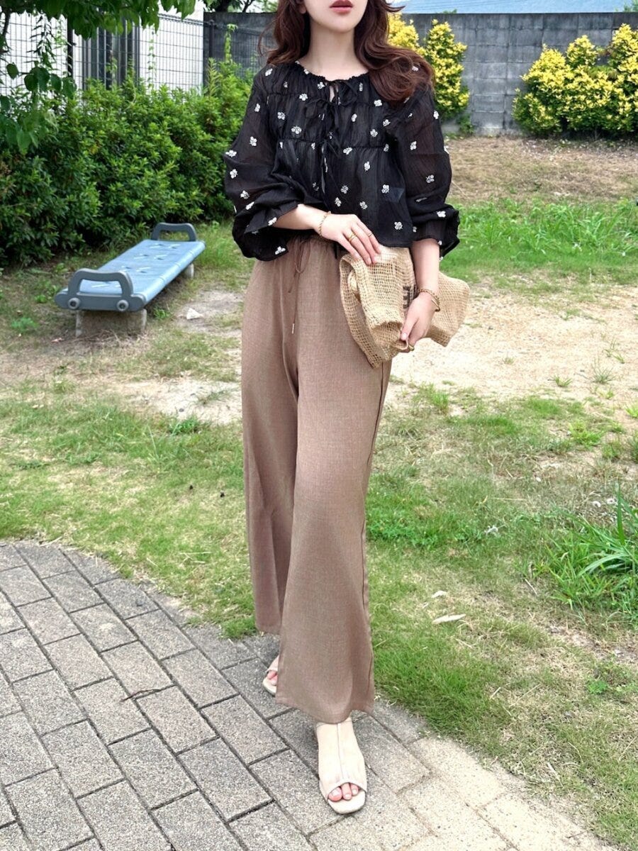 花柄シアー黒ブラウスとブラウンのワイドパンツを合わせた女性