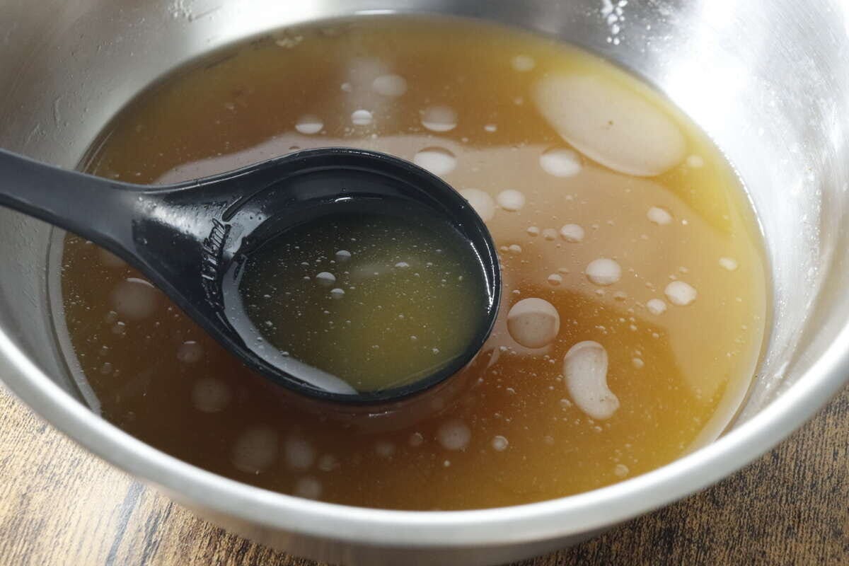 銀色のボウルに入ったラーメンスープの素を黒いお玉ですくっている様子 銀色のボウルに入ったラーメンスープの素を黒いお玉ですくっている様子