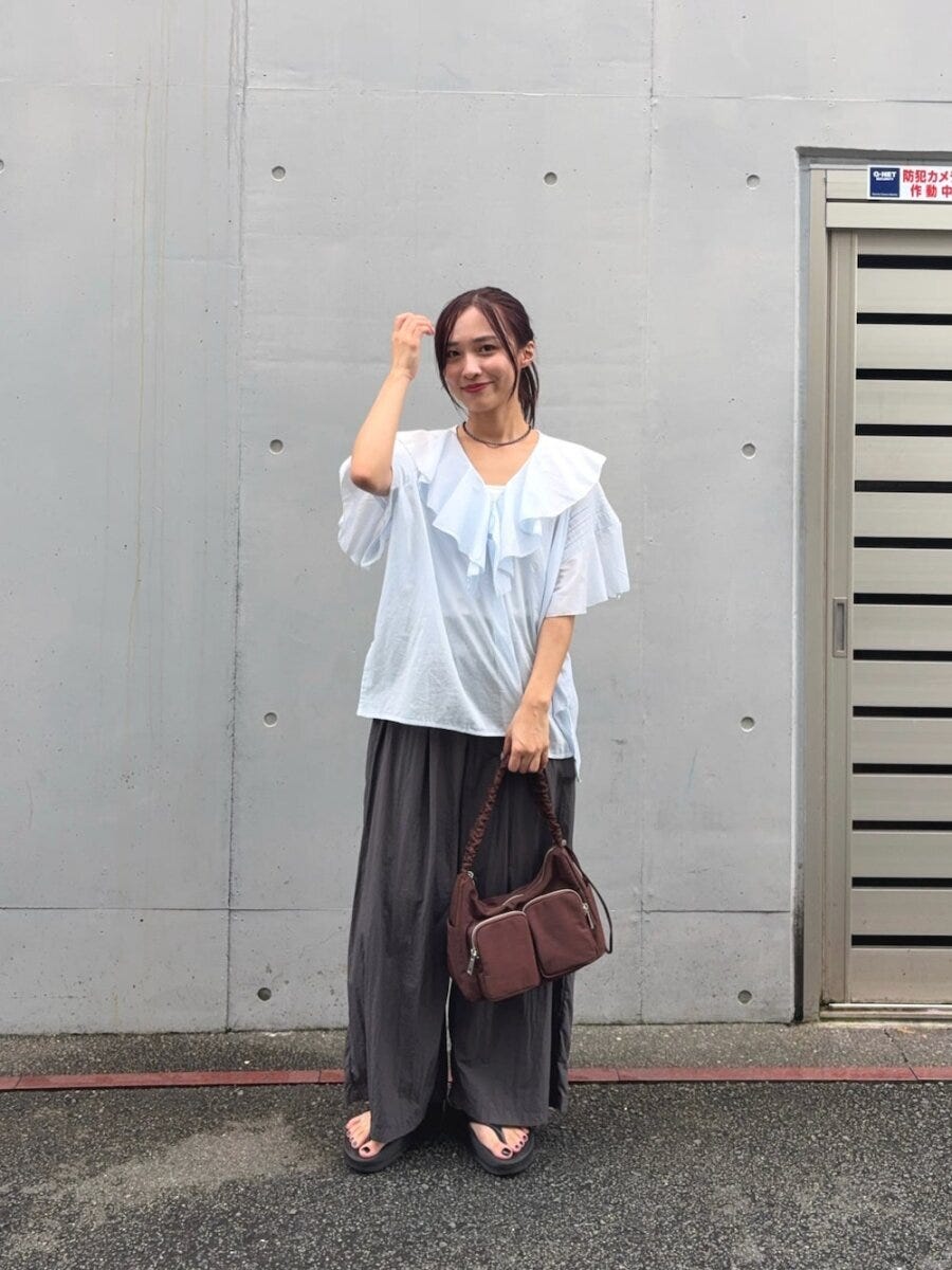 水色フリルブラウスとグレーパンツの女性が髪に手を添える