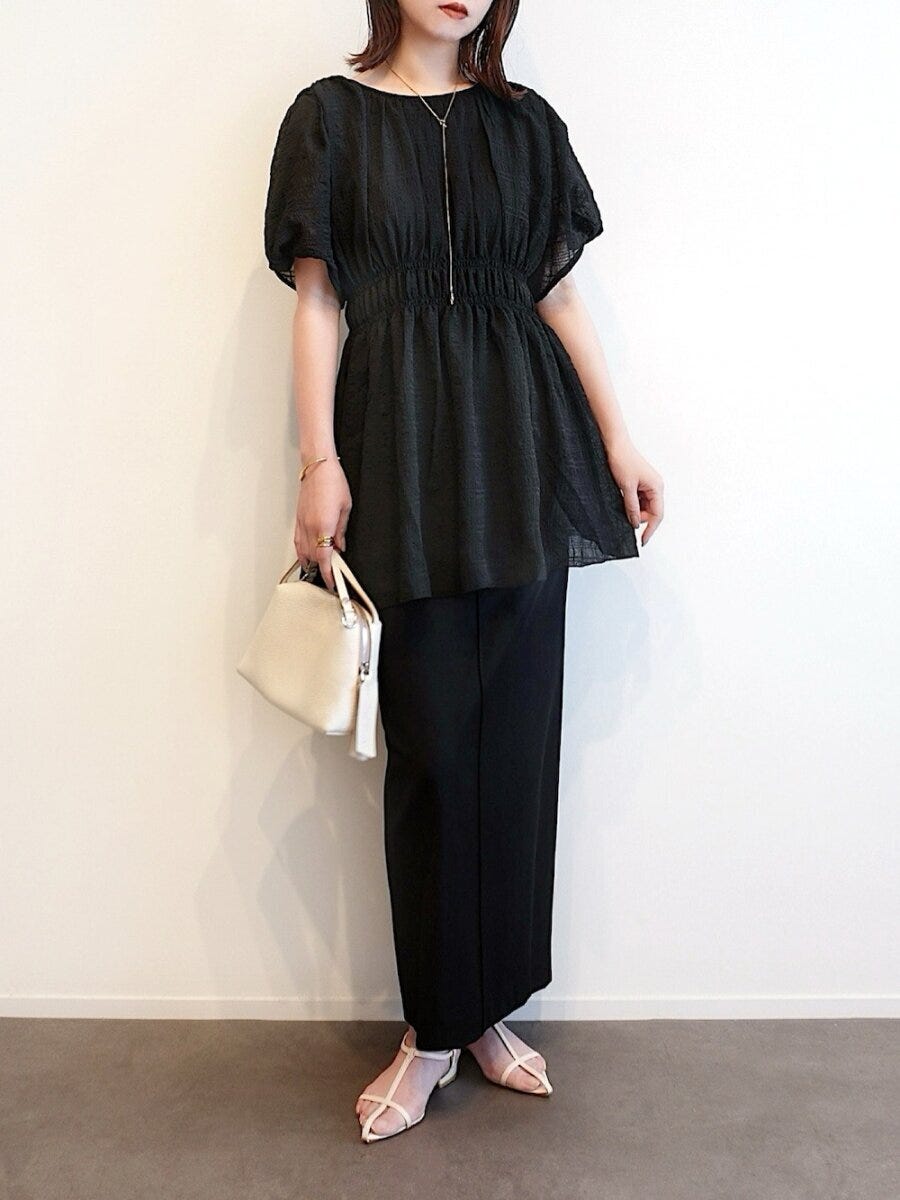 黒いブラウスとタイトスカートを着て白いバッグを持つ女性