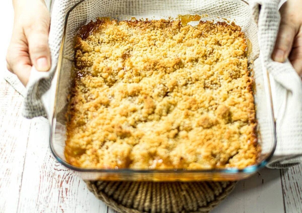 透明なガラス耐熱皿に焼き上がったりんごのクランブルを白いキッチンクロスで両手で持っている様子