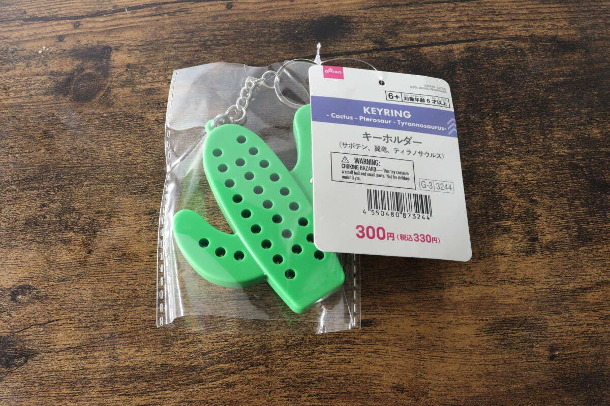 透明な袋に入った緑色のサボテン型キーホルダーと商品タグが木目のテーブルに置かれている 透明な袋に入った緑色のサボテン型キーホルダーと商品タグが木目のテーブルに置かれている