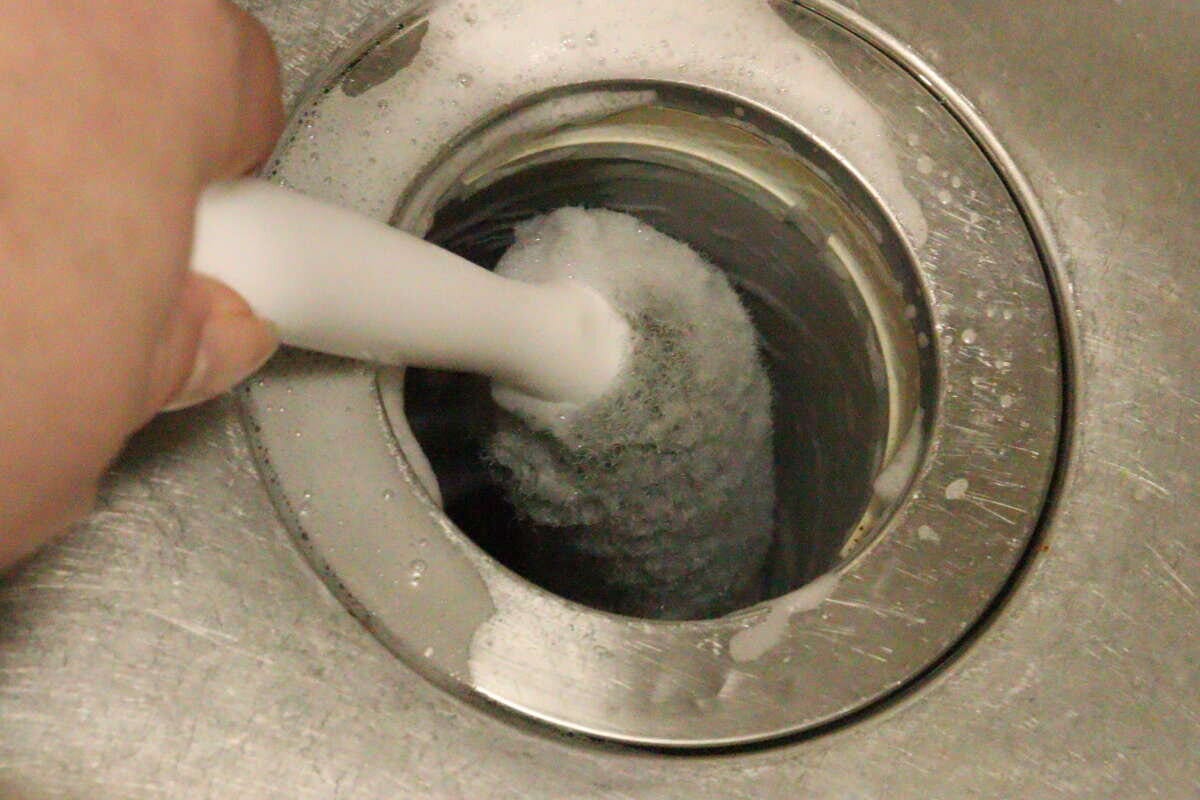 排水バスケットクリーナーでキッチンの排水口のワントラップ内部を泡立てながら掃除している様子